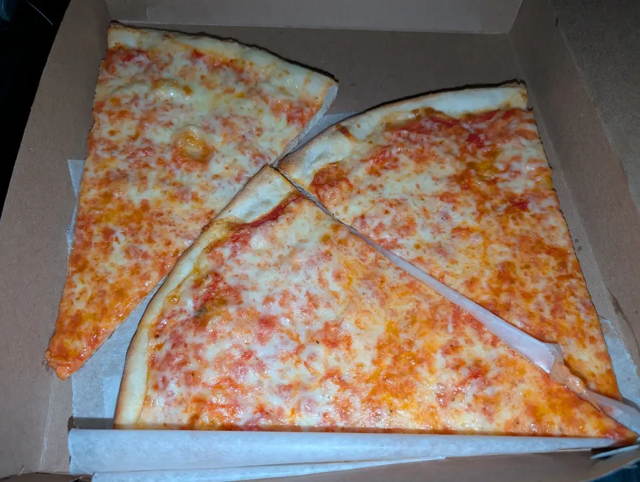 Three plain New York slices in an open pizza box on wax paper