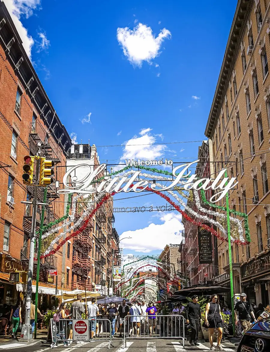 The “Welcome to Little Italy” sign and red, white and green garlands strung over Mulberry Street, with people walking below