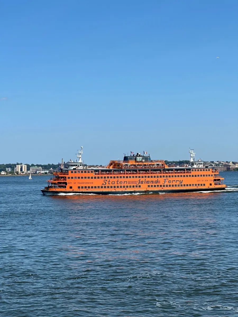 An orange Staten Island Ferry crossing the harbor under a clear blue sky
