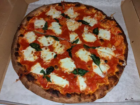 A charred-crust margherita in an open pizza box, with patches of fresh mozzarella and basil over bright tomato sauce