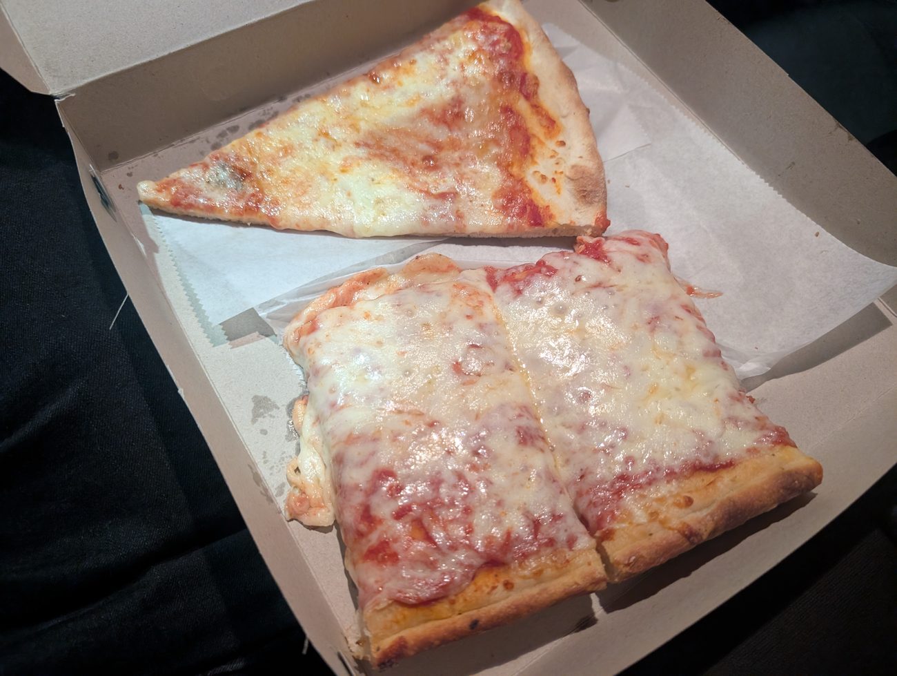 An open Pizza Wagon box holding one triangular round slice and one thick square Sicilian slice side by side.