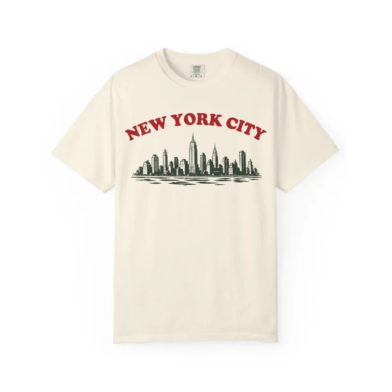 A cream t-shirt reading New York City over an illustration of the Manhattan skyline