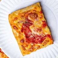 A grandma slice with crisp golden crust and sauce drizzled on top