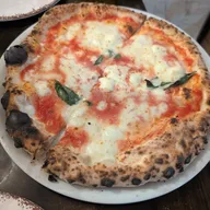 A whole Neapolitan margherita pie with charred, puffy crust and fresh basil