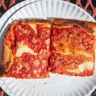 Two upside-down squares, sauce on top of the cheese, on a paper plate